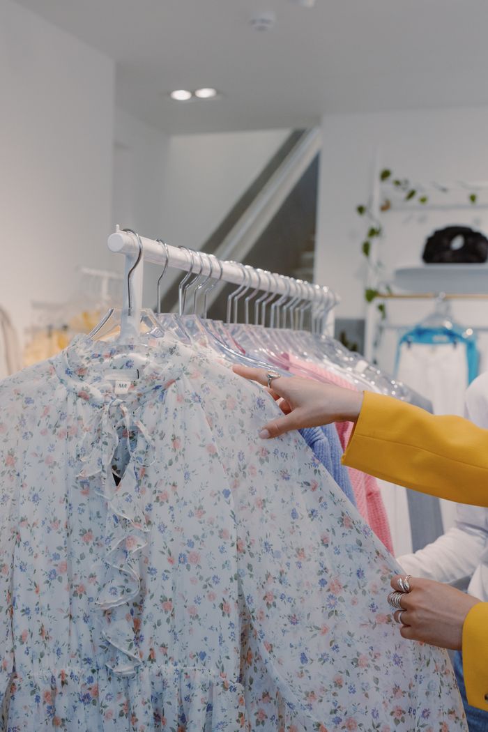 The Art of Drawing Readers In: Your attractive post title goes here Woman browsing floral print dresses on a clothing rack indoors in a fashion store.